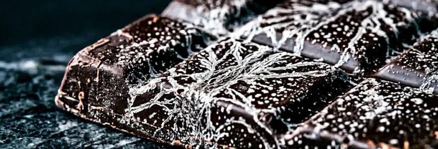 Tablette de chocolat noir avec effet de marbrure blanche caractéristique du fat bloom sur une surface en marbre