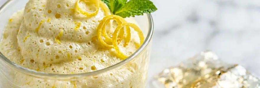Composition photographique épurée montrant une mousse au citron aérienne dans un verre transparent avec des citrons frais coupés et de la gélatine dorée en arrière-plan